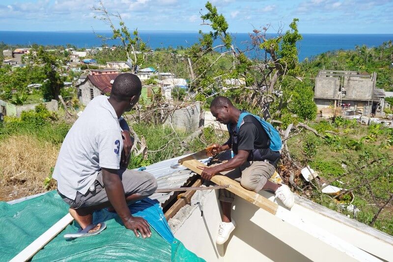 Team members rebuild Simon's roof with the ocean in back