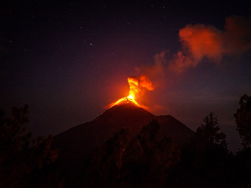An eruption lights up the night sky orange.