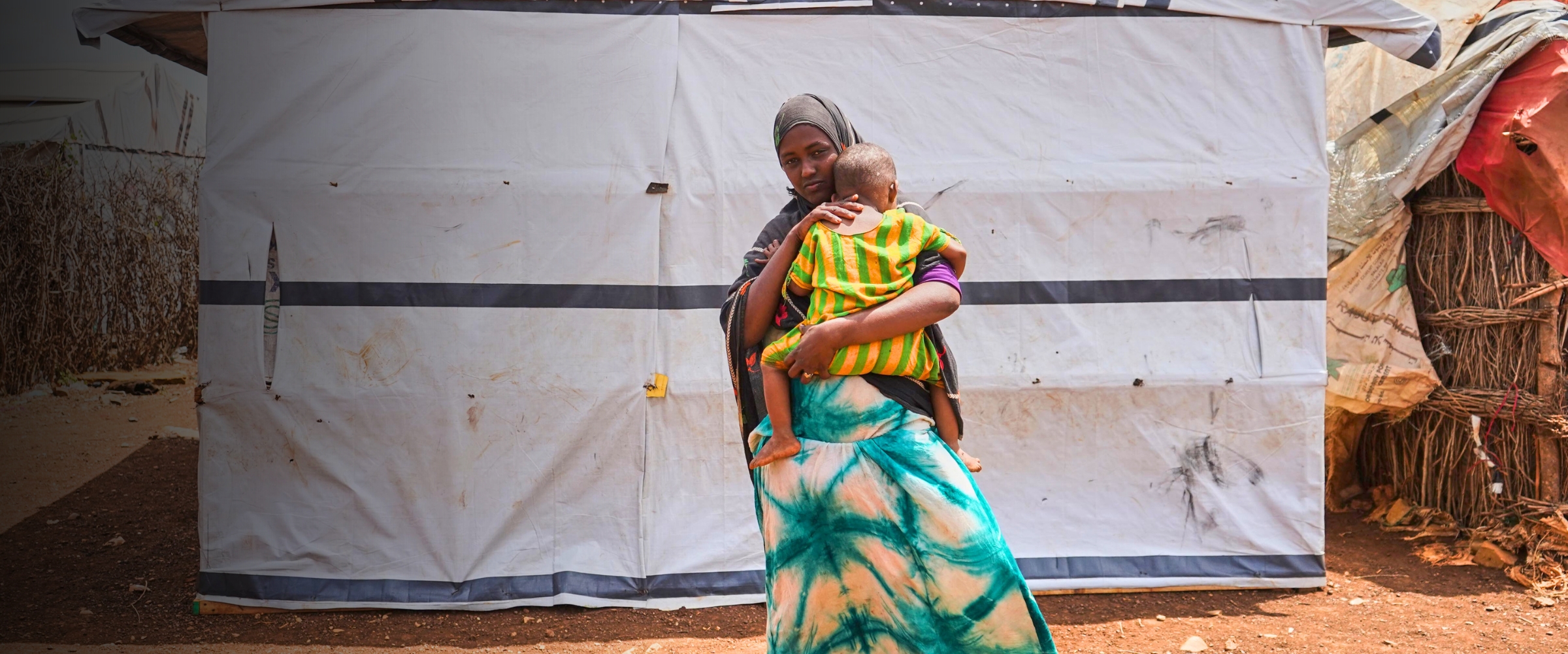 Woman holding child in front of temporary shelter.