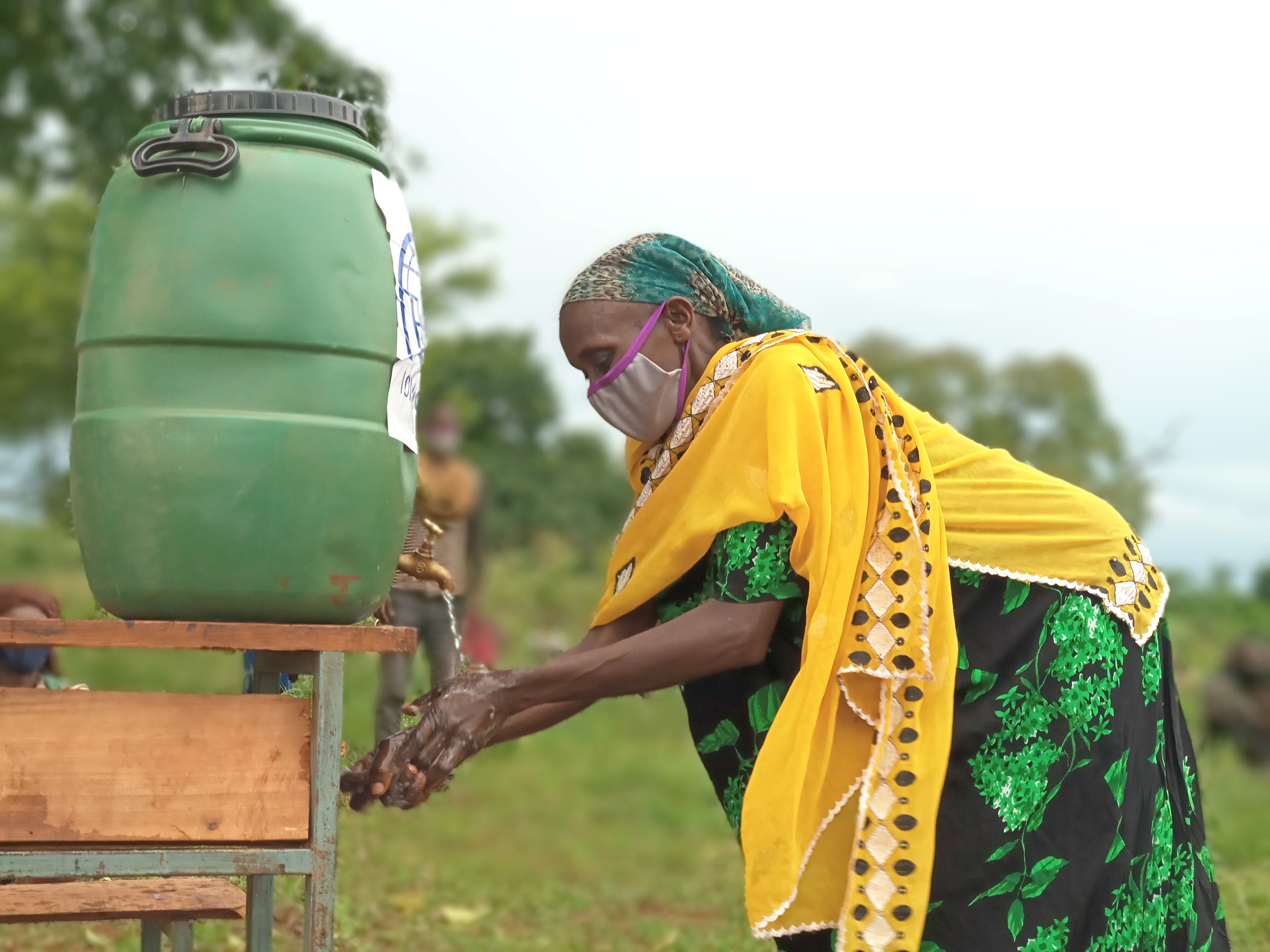 In Ethiopia, a woman wearing a face mask washes her hands a a water butt