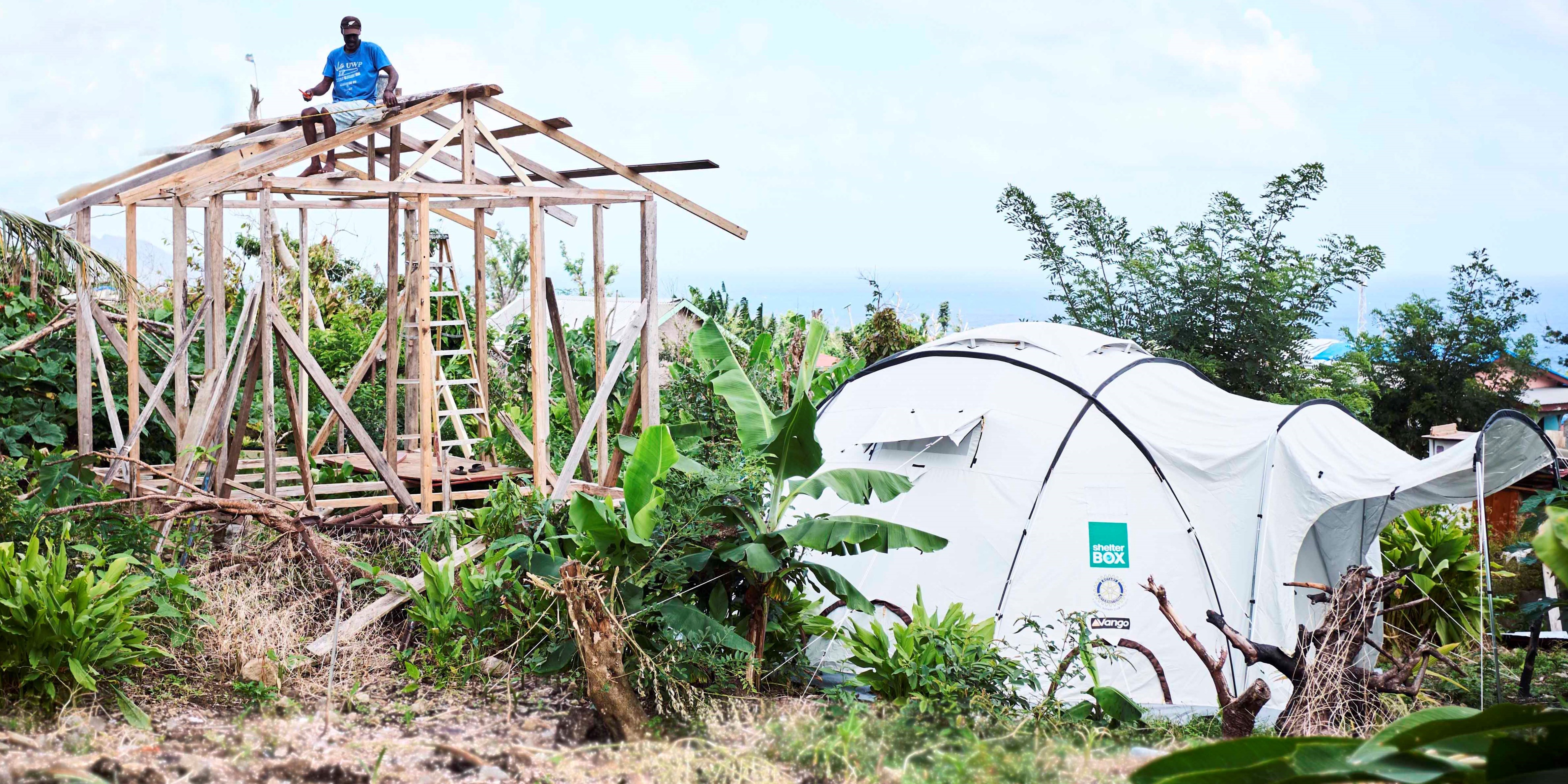 White ShelterBox tent in front of a wooden house frame