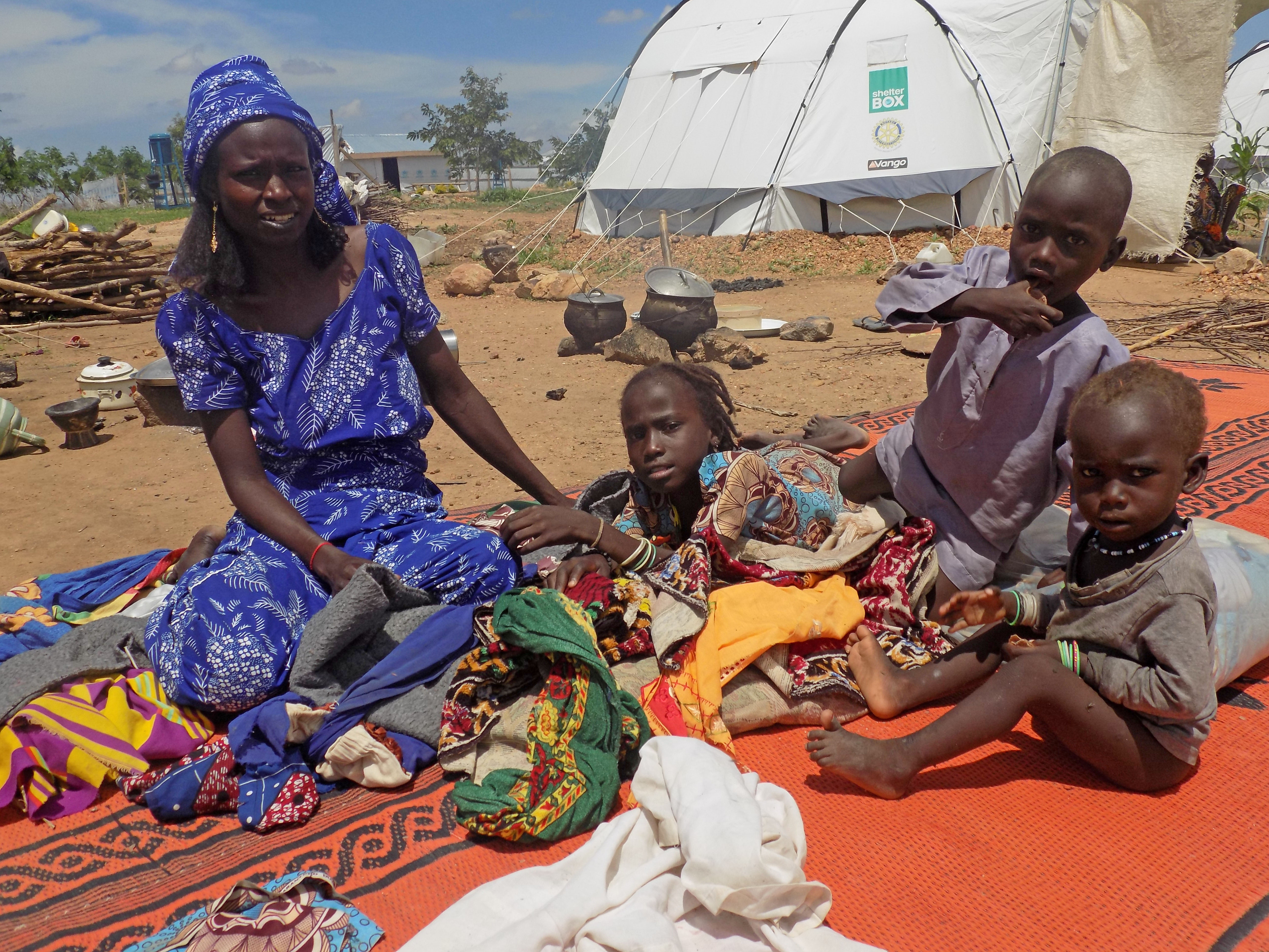 Fanne sits on a blanket with her children. Behind them is a ShelterBox tent.