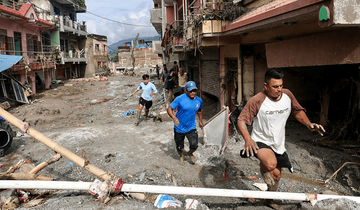 Local residents walk past houses lying deluged in sludge after flash floods at Devighat, Bidur Municipality in Nepal's Nuwakot district on August 27, 2026. Nepal's disaster agency said that 823 people remained out of contact on August 27, more than 24 hours after a deadly flood tore through the border region with Tibet.
